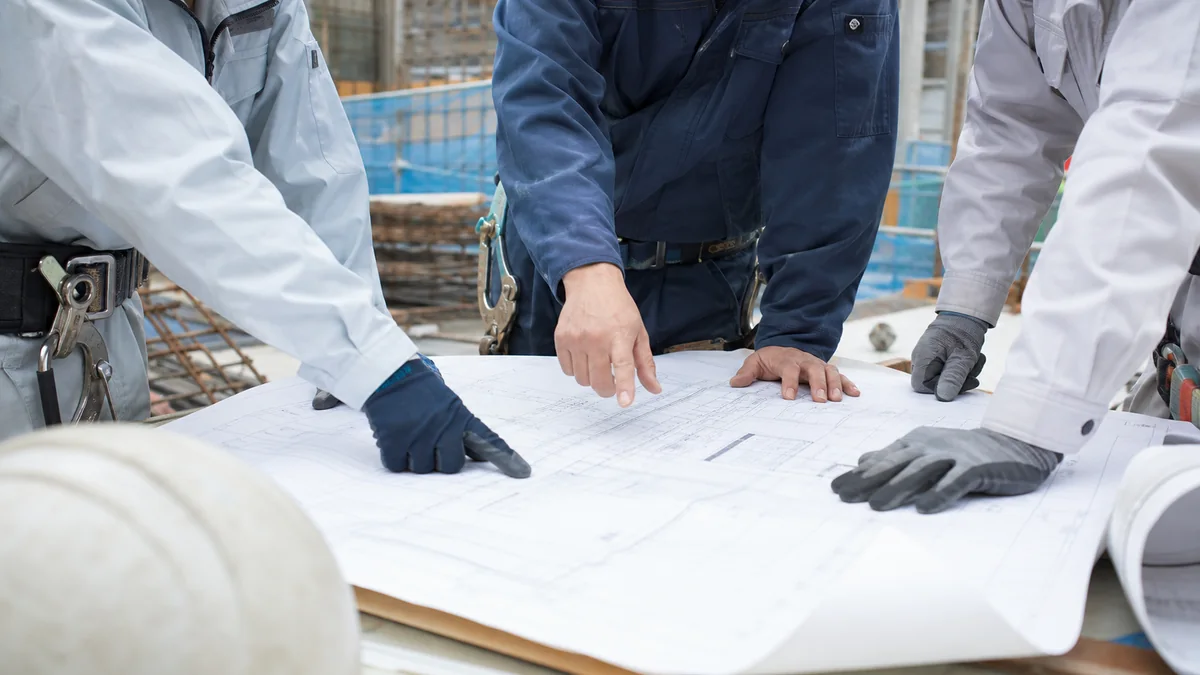 建設現場で図面を広げて打ち合わせをする複数の作業服の人たちの手元