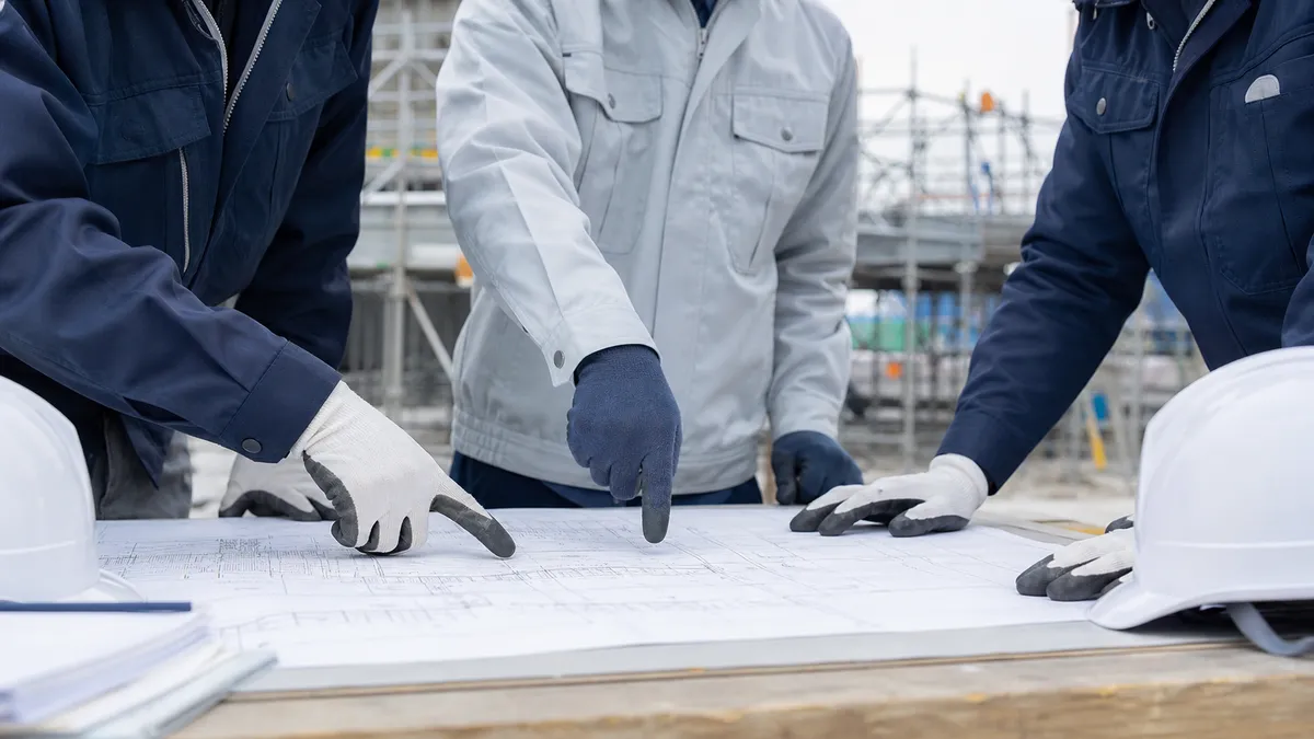 建設現場で図面を見ながら打ち合わせをする作業服の人たちの手元