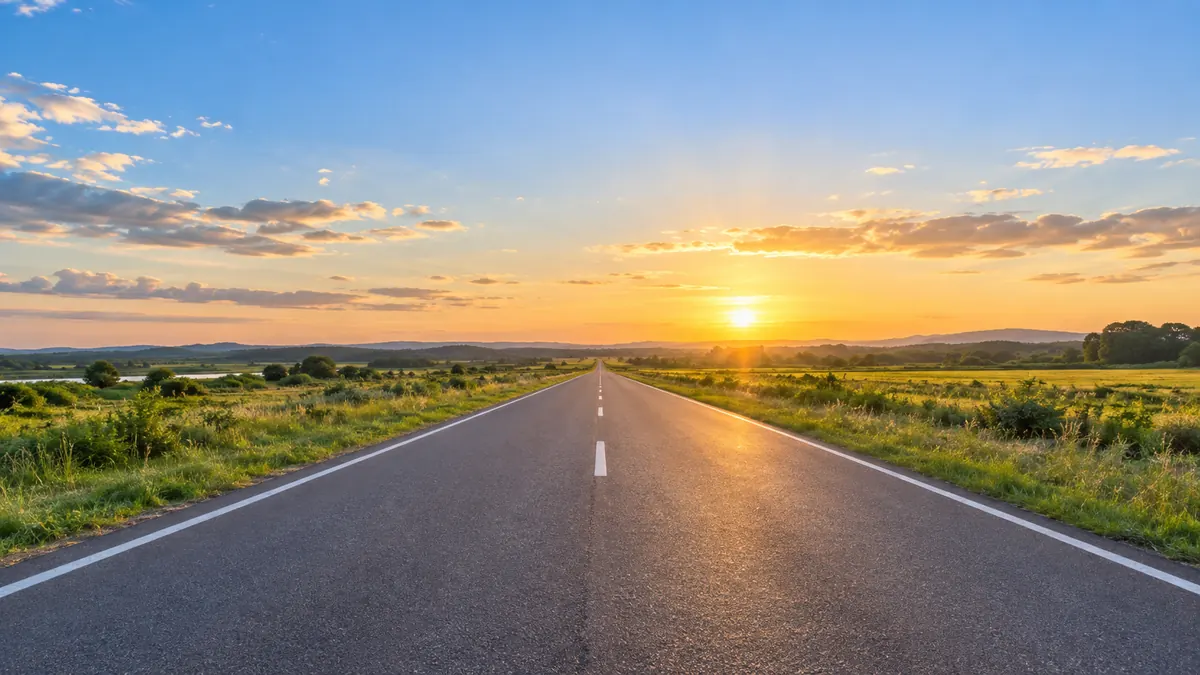 夕方の空の下、郊外の道路がまっすぐ先へ続いている景色